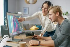 Male and Female Professional Editors Talk while Working in Photo Editing App / Software on a Personal Computer. Photo Editors Retouching Photos of a Beautiful Girl. Mock-up Software Design. Female Points at the Screen.